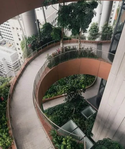 An elevated, spiraling walkway surrounded by lush greenery inside an urban building